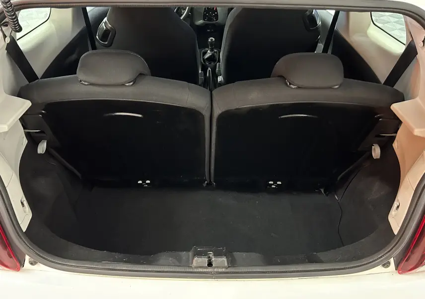 Vue depuis le coffre ouvert d'une Peugeot 108 blanche, montrant l'intérieur noir des sièges arrière et la boîte manuelle.
