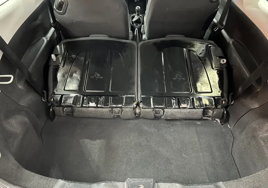 Vue du coffre arrière d'une Peugeot 108 blanche avec banquette arrière rabattue, montrant l'espace de chargement et l'intérieur noir.