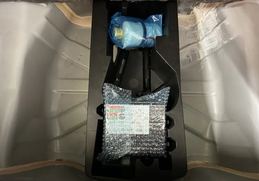 Vue plongeante sur le coffre d’une Peugeot 108 blanc, montrant un rangement avec outils emballés sous plastique et film bulle.