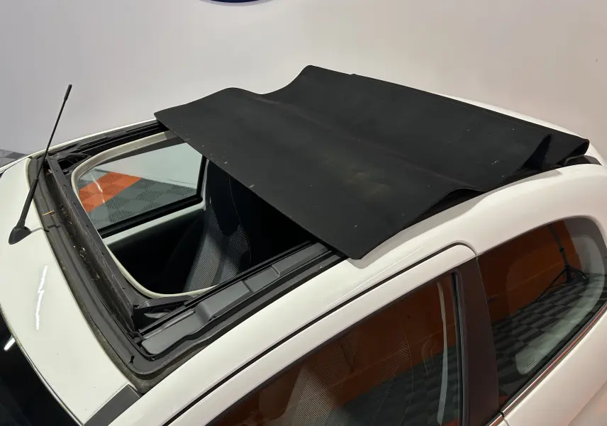 Vue rapprochée du toit ouvrant en toile noire déployé sur une Peugeot 108 blanche, intérieur partiellement visible.