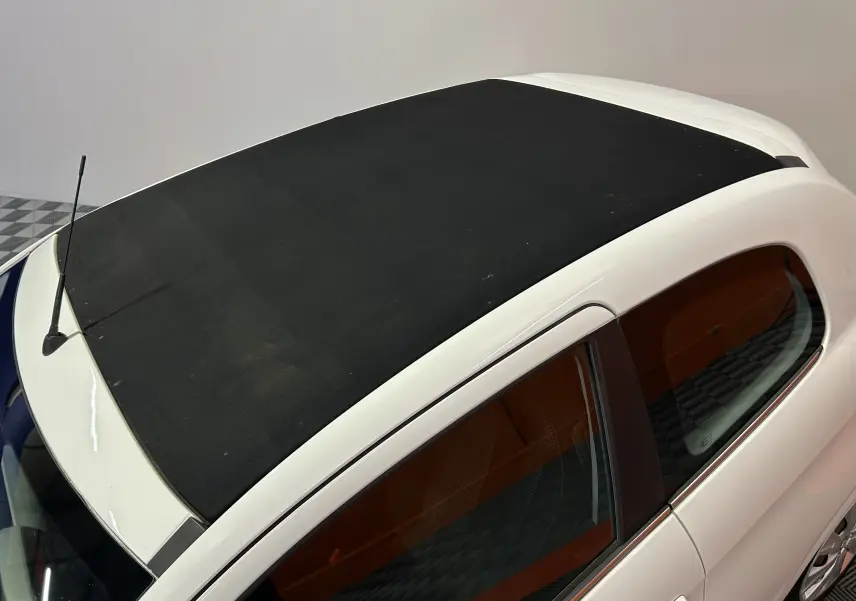 Vue plongeante sur le toit ouvrant en toile noire d'une Peugeot 108 blanche, avec partie latérale droite visible.