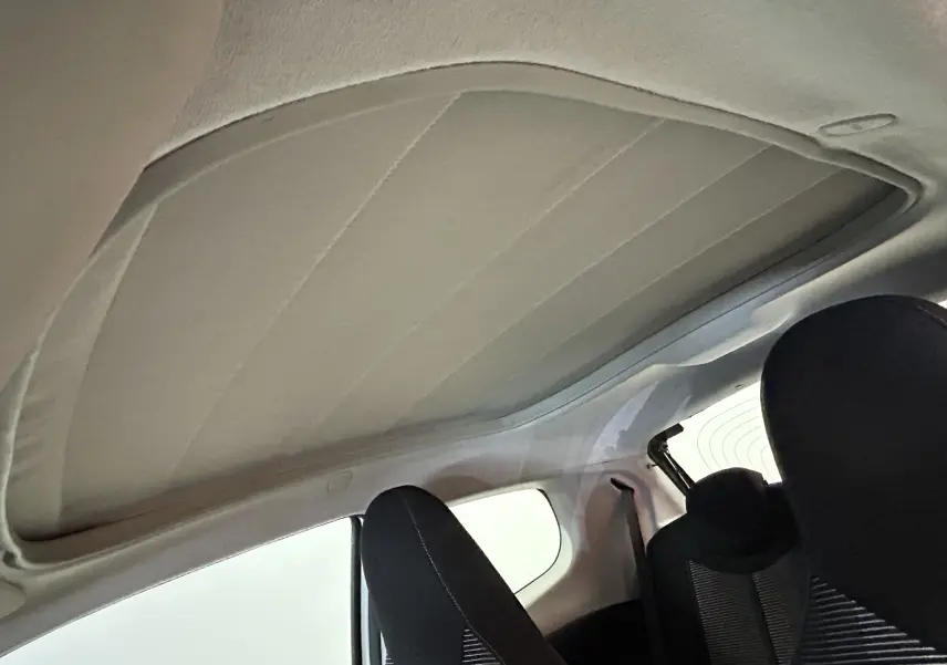 Toit ouvrant en tissu beige vu de l'intérieur arrière d'une Peugeot 108 blanche, sièges noirs visibles.