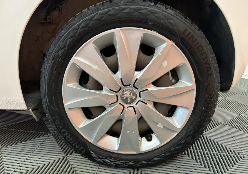 Gros plan sur la roue avant droite d’une Peugeot 108 blanche avec jante argentée et traces d’usure visibles.