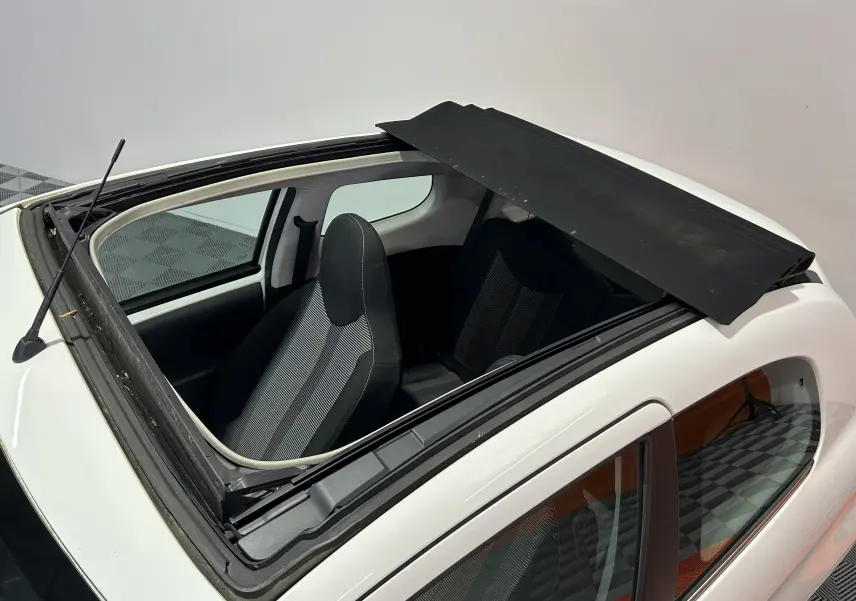 Vue plongeante sur le toit ouvrant ouvert d'une Peugeot 108 blanche, montrant les sièges avant en tissu noir et gris.