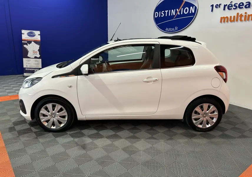 Vue latérale droite d'une Peugeot 108 blanche 2014 avec toit ouvrant partiellement ouvert dans un showroom.