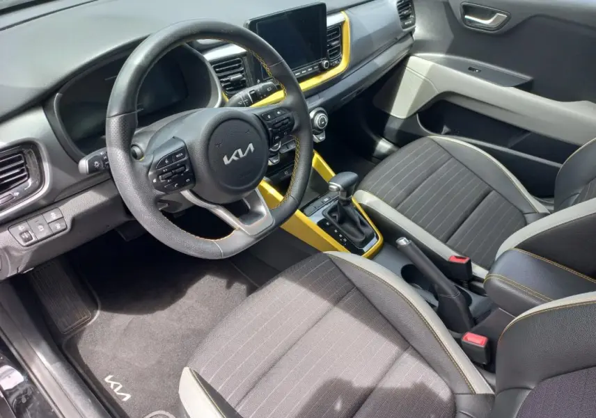 Vue intérieure côté conducteur du Kia Stonic 2025 avec sellerie noire, volant multifonction et inserts jaunes autour de la console centrale.
