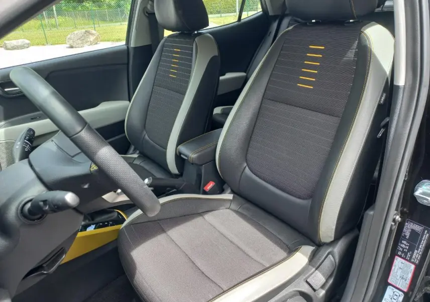 Vue intérieure côté conducteur du Kia Stonic noir 2025, sièges tissu avec surpiqûres jaunes et détails gris.