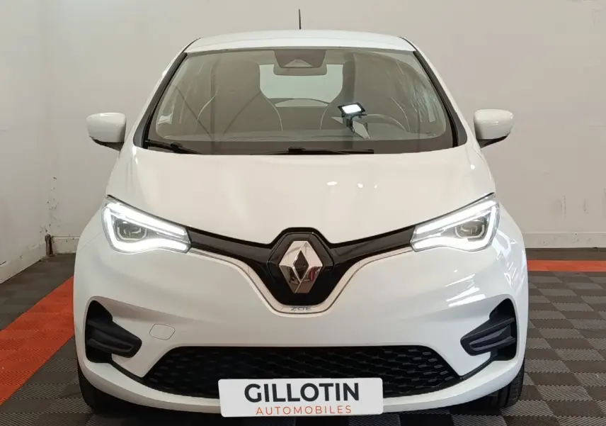 Vue de face de la Renault ZOE Business blanche 2021 avec phares LED allumés et calandre noire distinctive.
