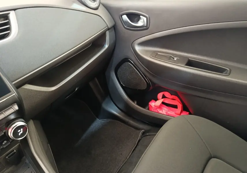 Intérieur côté passager avant de la Renault ZOE blanche, avec porte noire et sac rose dans le rangement.