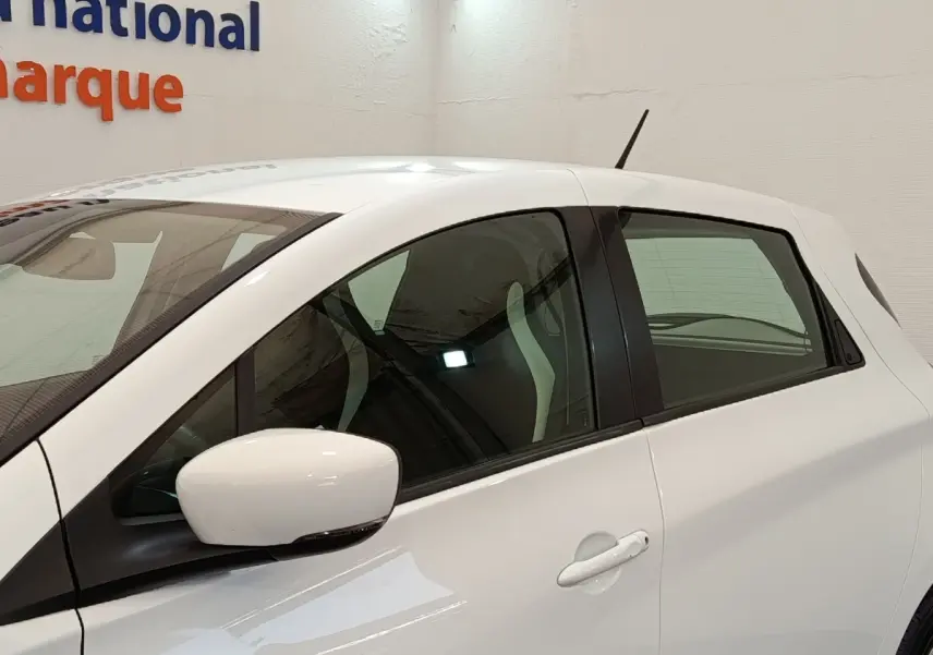 Vue latérale droite d'une Renault ZOE Business blanche, avec rétroviseur et poignées assortis, intérieur partiellement visible.