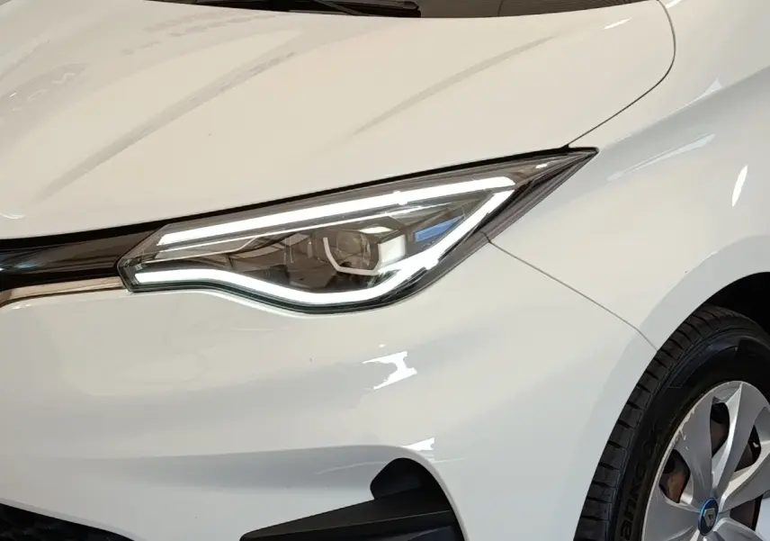 Gros plan sur le phare avant droit blanc de la Renault ZOE 2021 avec jante alu et carrosserie lisse.