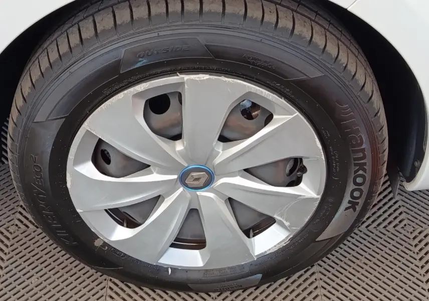 Gros plan sur la roue avant droite blanche d'une Renault ZOE 2021 avec jante abîmée et logo Renault central.