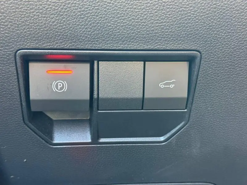 Gros plan sur les boutons de commande du frein à main électronique et du coffre dans l'habitacle du Dacia Bigster gris Schiste.