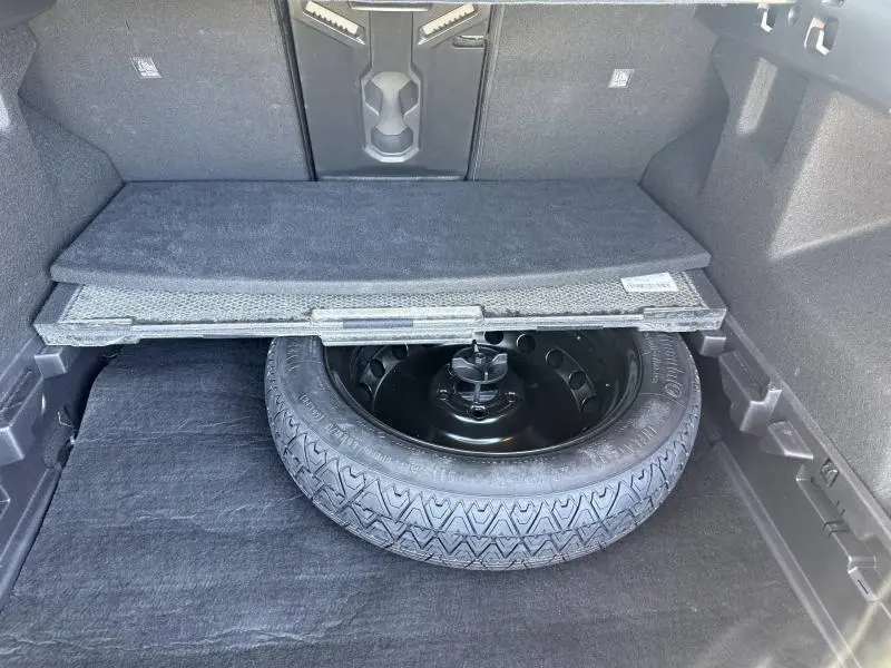 Coffre ouvert du Dacia Bigster gris Schiste montrant la roue de secours sous le plancher de coffre.