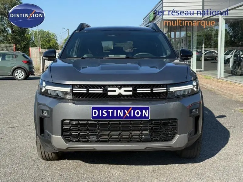 Vue frontale d'un Dacia Bigster gris schiste avec calandre noire et logo central distinctif, stationné en extérieur.