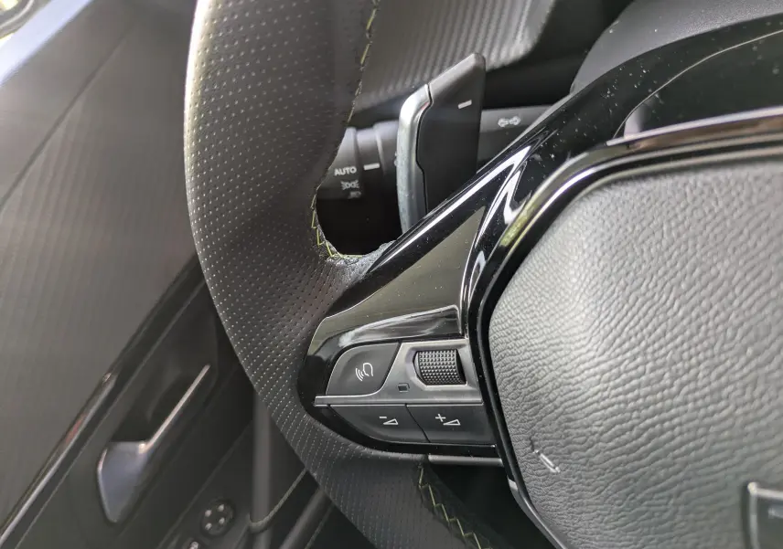 Gros plan sur la partie gauche du volant en cuir perforé noir avec surpiqûres vertes du Peugeot 208 Hybrid 145 GT 2025.