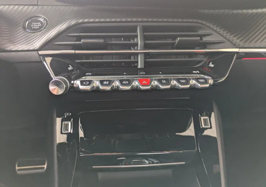 Vue rapprochée de la console centrale noire brillante du Peugeot 208 Hybrid 145, avec commandes tactiles et bouton start/stop.