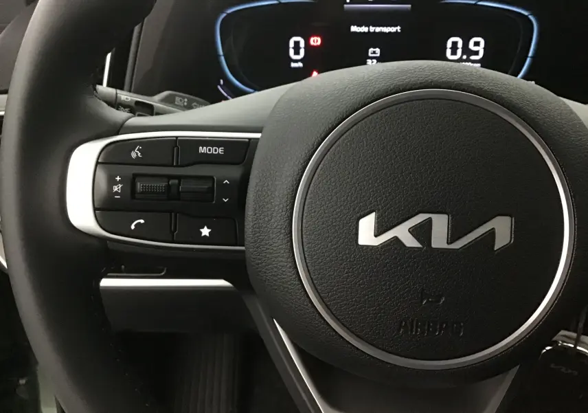 Gros plan sur le volant cuir du Kia Sportage 2025 avec commandes intégrées et tableau de bord digital lumineux.