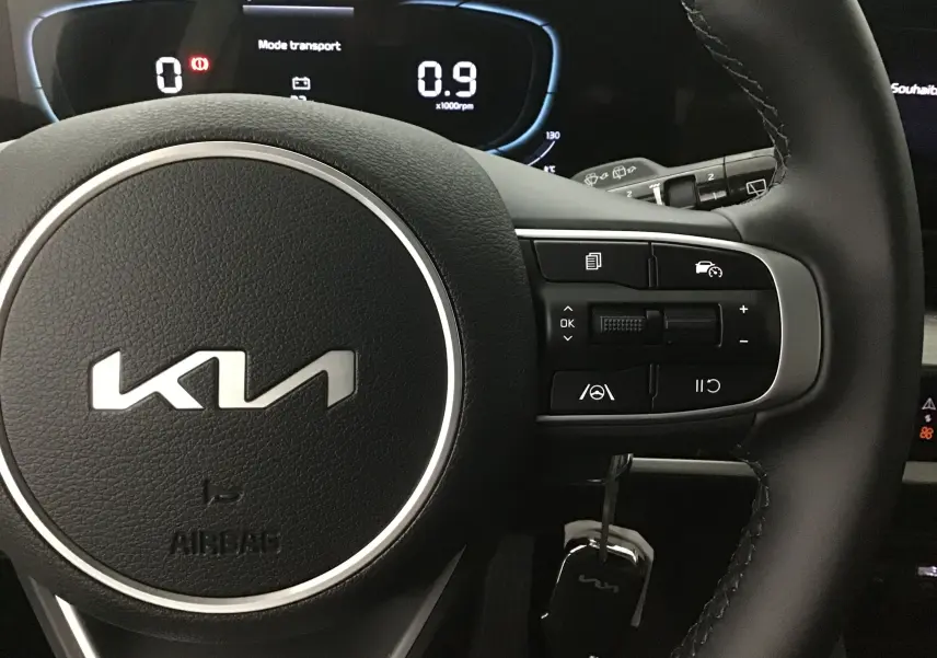 Gros plan sur le volant cuir du Kia Sportage 2025 avec commandes multifonctions et tableau de bord digital lumineux.