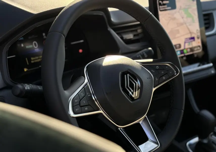 Vue rapprochée du volant noir de la Renault Captur 2025 avec commandes intégrées et écran tactile en arrière-plan.
