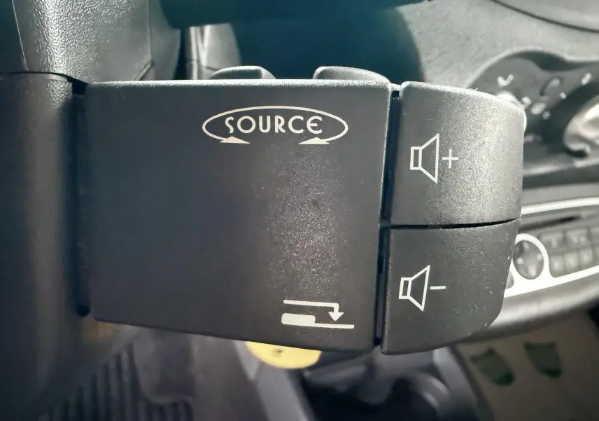 Gros plan sur les commandes audio au volant d’une Renault Twingo II grise, intérieur tissu gris.
