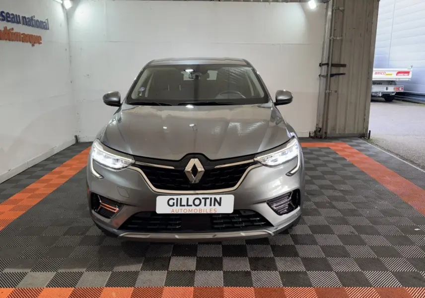 Vue avant d’un Renault Arkana Business E-TECH 145 gris foncé avec phares LED allumés dans un garage.