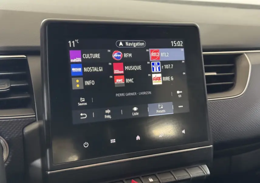 Écran tactile central affichant les stations radio dans l’habitacle d’une Renault Arkana gris foncé, vue de face.