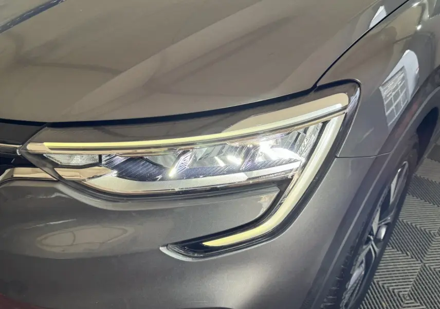 Gros plan sur le phare avant droit LED d’un Renault Arkana Business E-TECH gris foncé, avec partie de la roue visible.