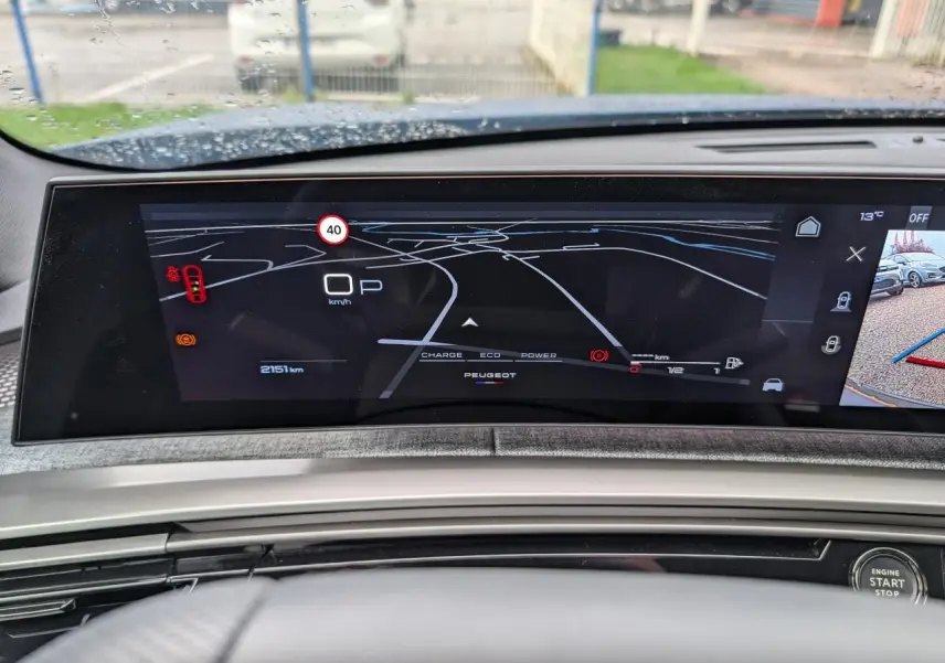 Vue rapprochée du tableau de bord numérique du Peugeot 3008 1.2i Hybrid 2025 avec affichage de navigation et caméra de recul.