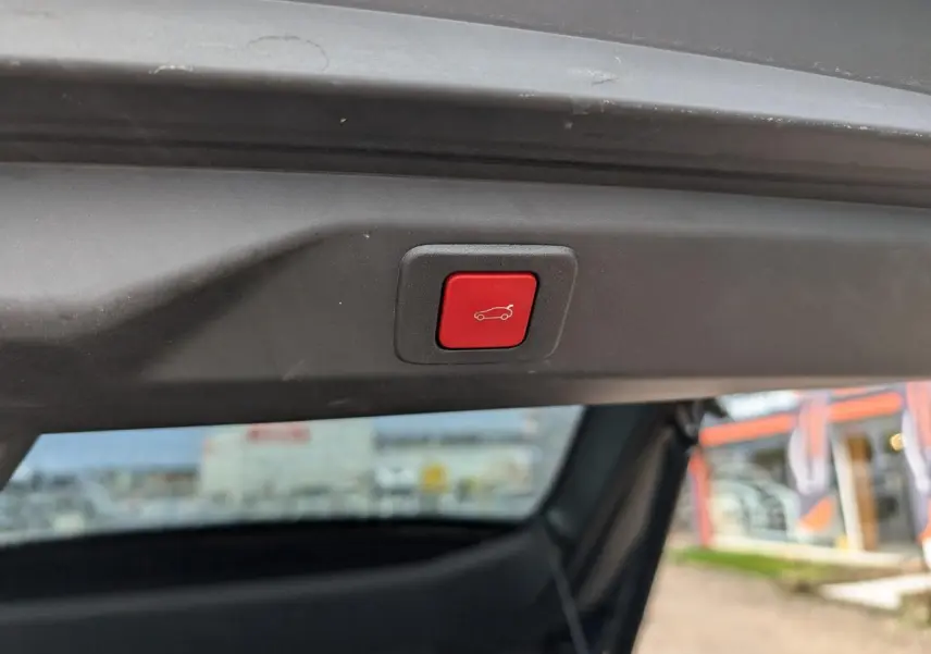 Bouton rouge d'ouverture électrique du hayon visible en gros plan sur un Peugeot 3008 bleu métallisé.