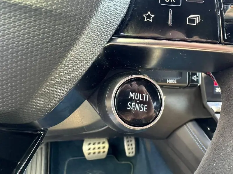 Gros plan sur le bouton Multi Sense noir brillant au tableau de bord du Renault Rafale 1.2 E-Tech bleu, avec pédalier sport visible.