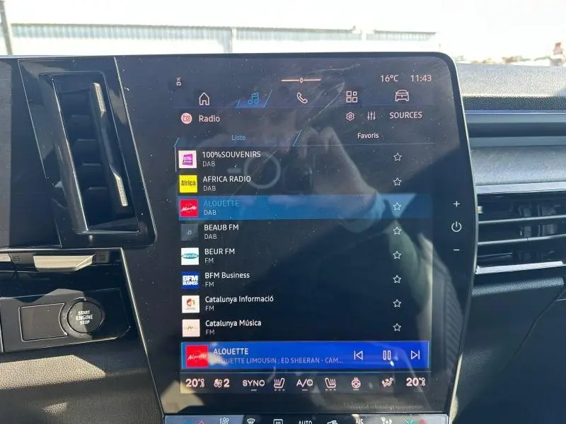 Vue rapprochée de l'écran tactile central du tableau de bord du Renault Rafale bleu Sommet, affichant les stations radio.
