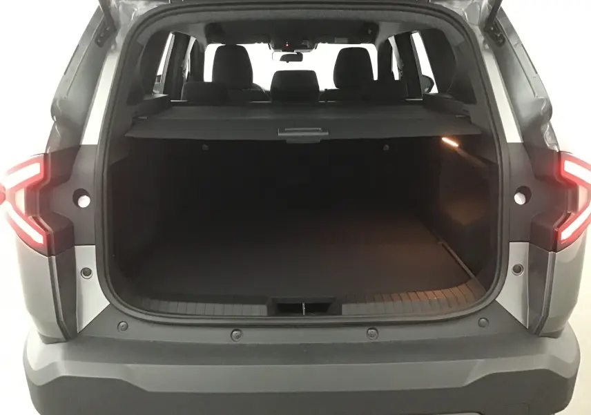 Coffre ouvert vu de l'arrière d'un Dacia Bigster gris schiste 2025 avec feux arrière allumés et intérieur spacieux.