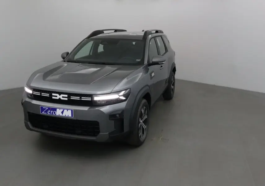 SUV Dacia Bigster gris schiste vu en 3/4 avant droit avec calandre lumineuse et barres de toit noires.