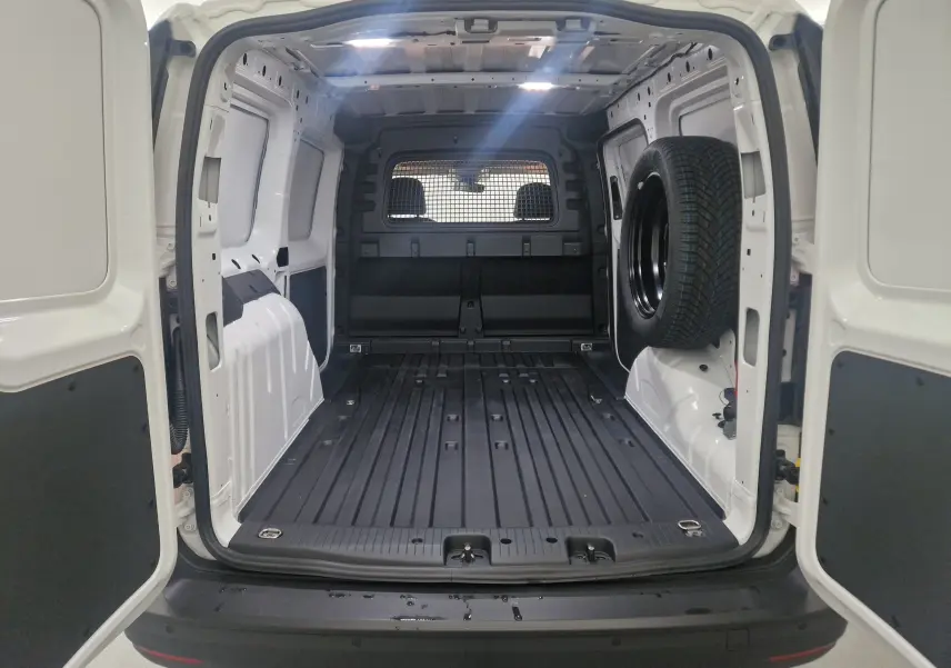 Vue arrière du Volkswagen Caddy Maxi blanc 2025, montrant l'espace de chargement vide avec roue de secours fixée à droite.