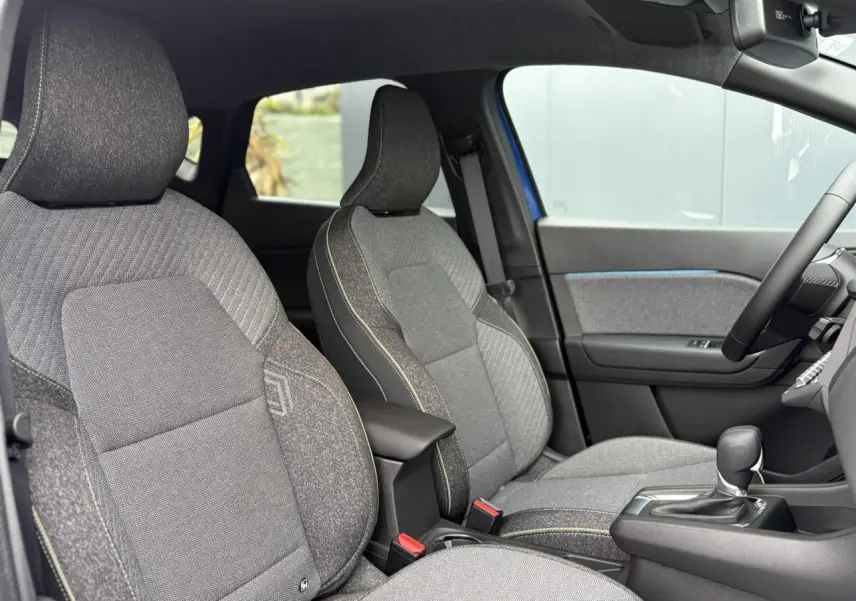 Vue intérieure côté conducteur du Renault Captur 2025, sièges gris texturés avec console centrale et volant textile.