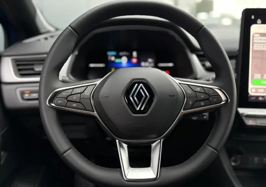 Gros plan sur le volant noir du Renault Captur 2025 avec commandes intégrées et logo central chromé.