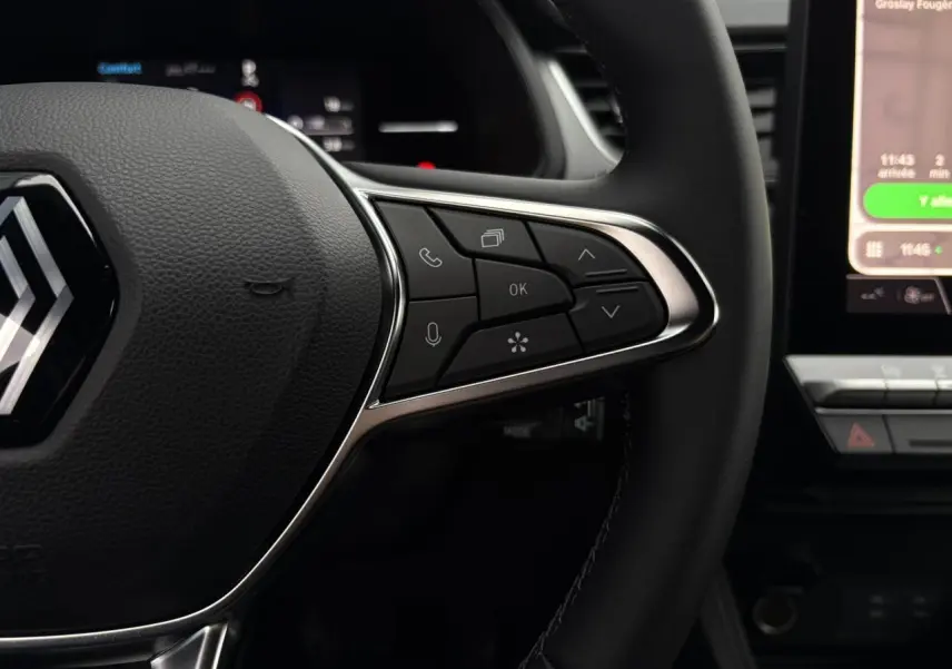 Gros plan sur le volant noir du Renault Captur 2025, avec commandes multifonctions et écran tactile partiel en arrière-plan.