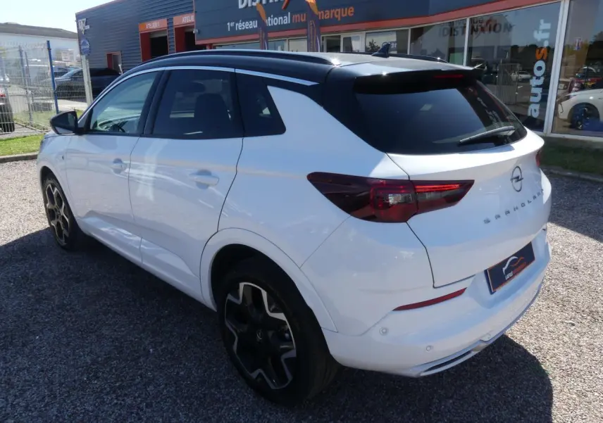 Opel Grandland blanc métallisé vu 3/4 arrière droit, toit noir brillant et jantes alliage noires distinctives.