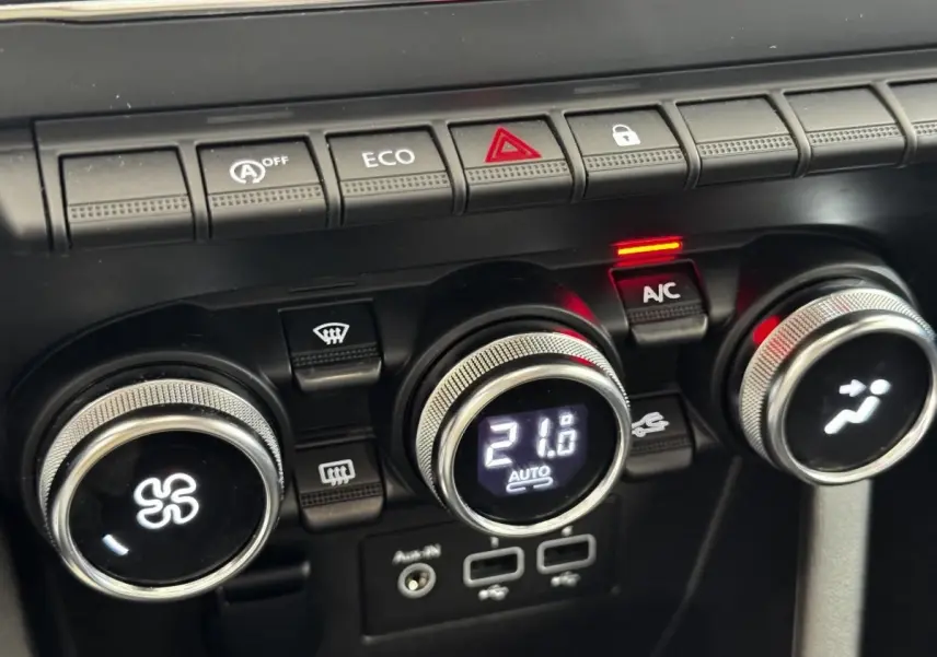 Gros plan sur les commandes de climatisation et boutons de fonction du tableau de bord d’une Renault Clio Business gris clair.