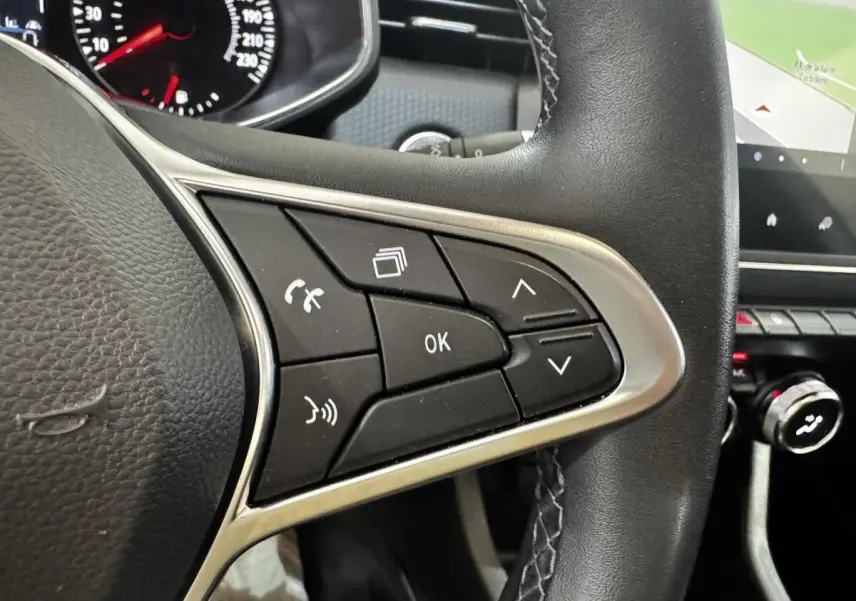 Gros plan sur le volant multifonctions en cuir synthétique de la Renault Clio Business TCe 100, avec commandes vocales et écran tactile visible.