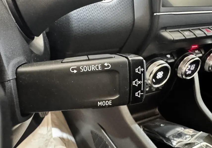 Gros plan sur la commande au volant gauche de la Renault Clio Business TCe 100, avec tableau de bord noir et boutons de climatisation visibles.