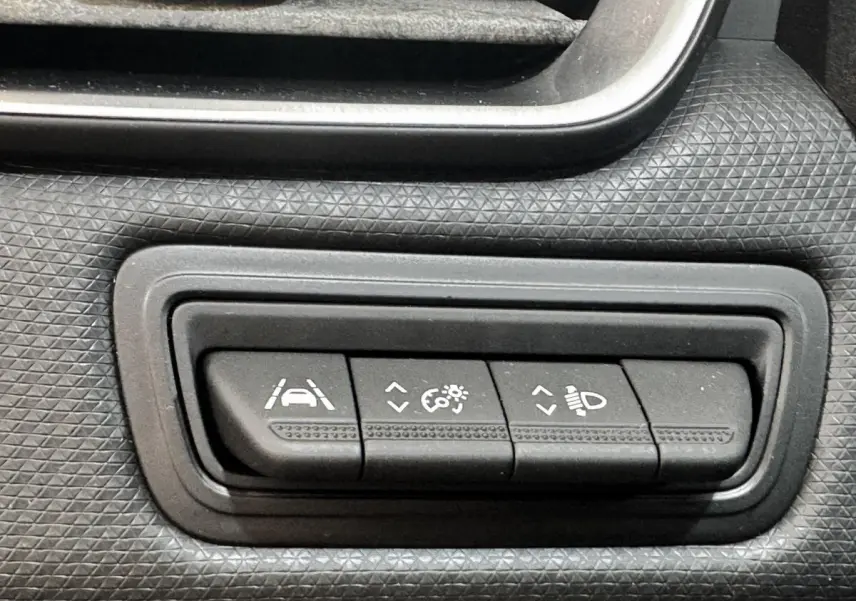Gros plan sur les boutons de réglage des aides à la conduite et des phares dans une Renault Clio Business gris clair de 2020.