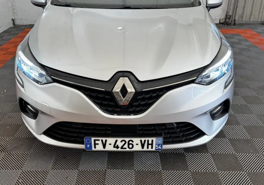 Vue avant rapprochée d’une Renault Clio Business TCe 100 gris clair avec phares LED allumés et calandre noire.