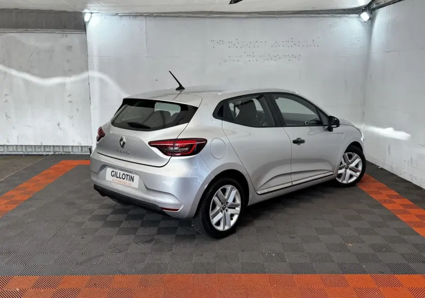 Renault Clio Business TCe 100 gris clair vue 3/4 arrière droit dans un garage avec sol noir et orange.