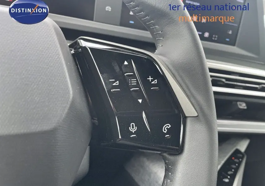 Gros plan sur les commandes gauche du volant cuir noir du Peugeot 3008 Hybrid 2025 avec écran tactile en arrière-plan.