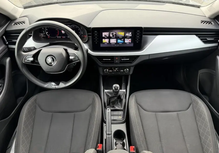 Intérieur du Skoda Kamiq 2023 vu de face, tableau de bord moderne avec écran tactile et sièges tissu noirs.