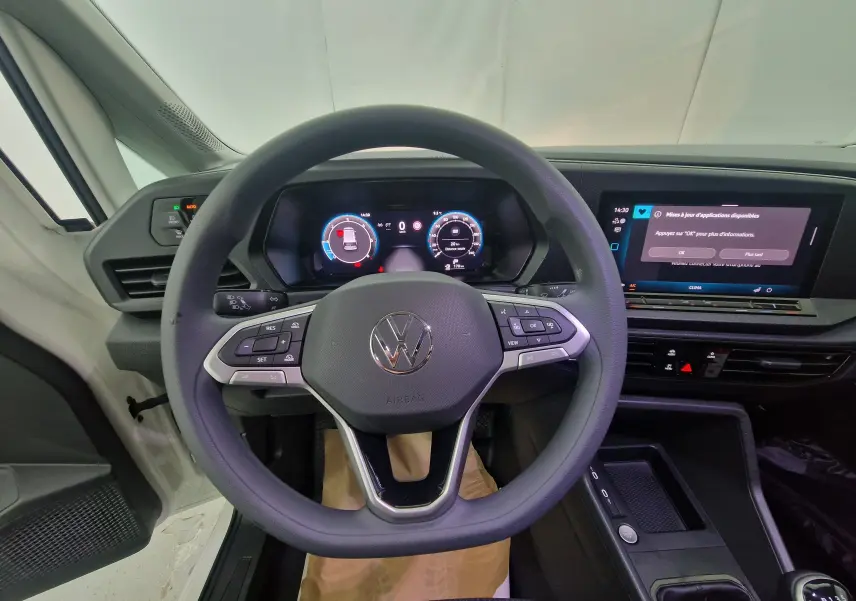 Vue intérieure côté conducteur du Volkswagen Caddy Maxi blanc, montrant les sièges avant et le tableau de bord moderne.