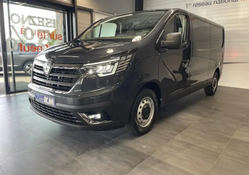 Renault Trafic Fourgon gris Comète en vue 3/4 avant droit, avec projecteurs Full LED allumés en showroom.