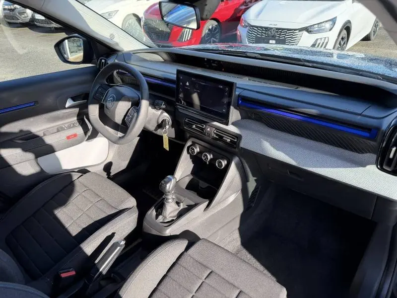 Vue intérieure côté conducteur de la Citroën C3 1.2 Turbo 100ch Plus 2025, avec tableau de bord noir et écran tactile central.